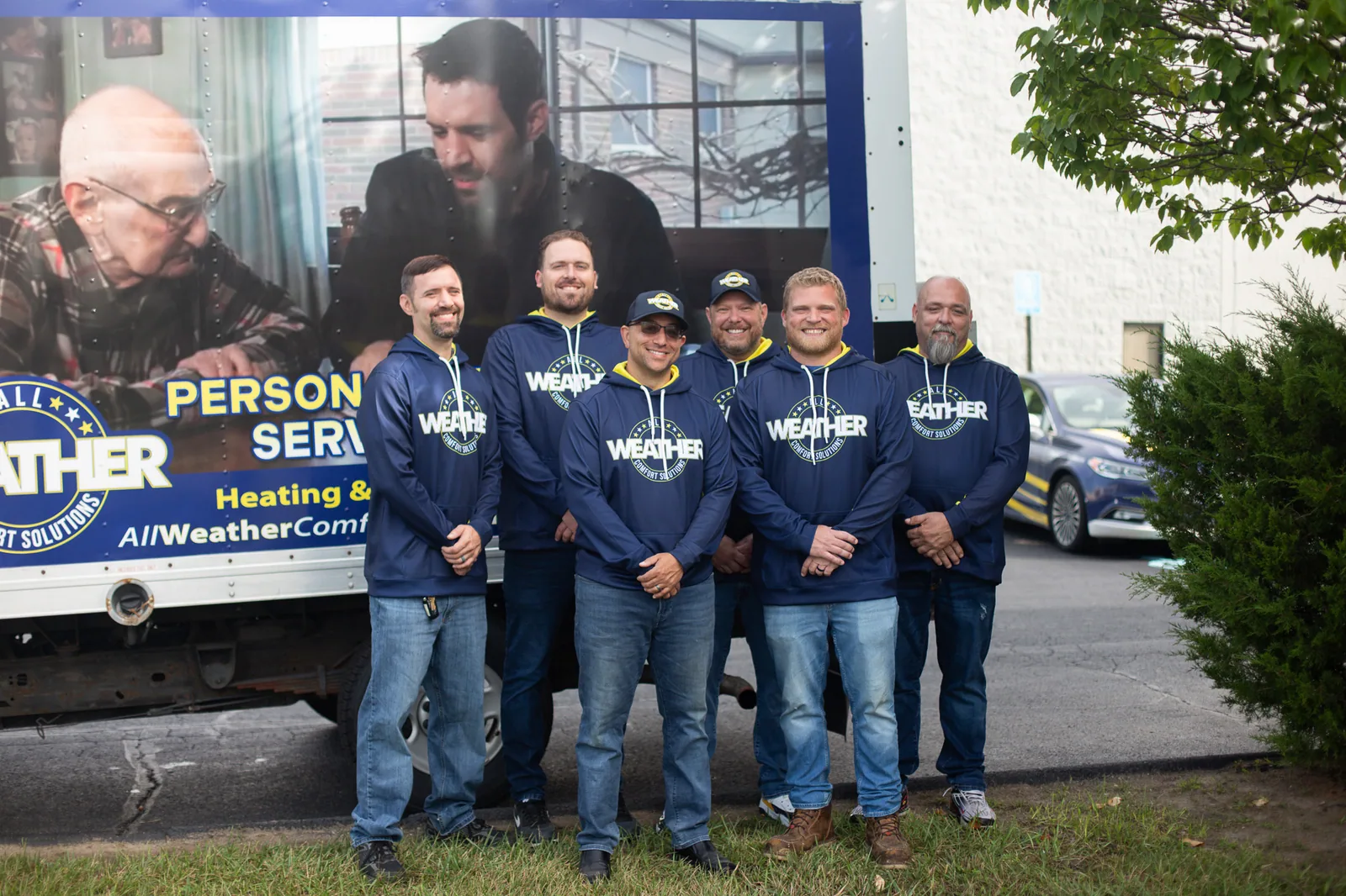 Six All Weather Comfort Solutions team members smiling beside a branded company truck