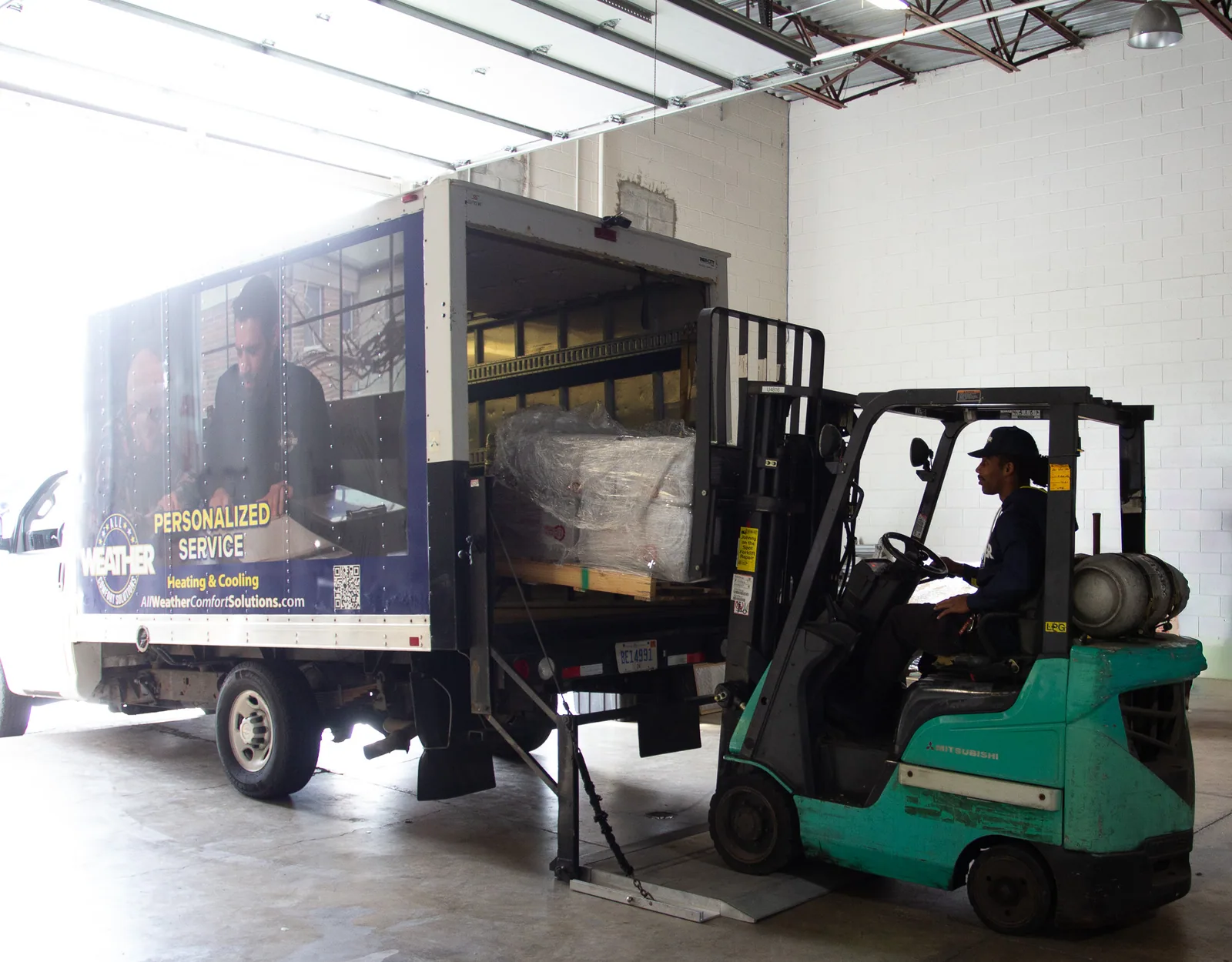 A forklift loading wrapped equipment into an All Weather box truck at the shop