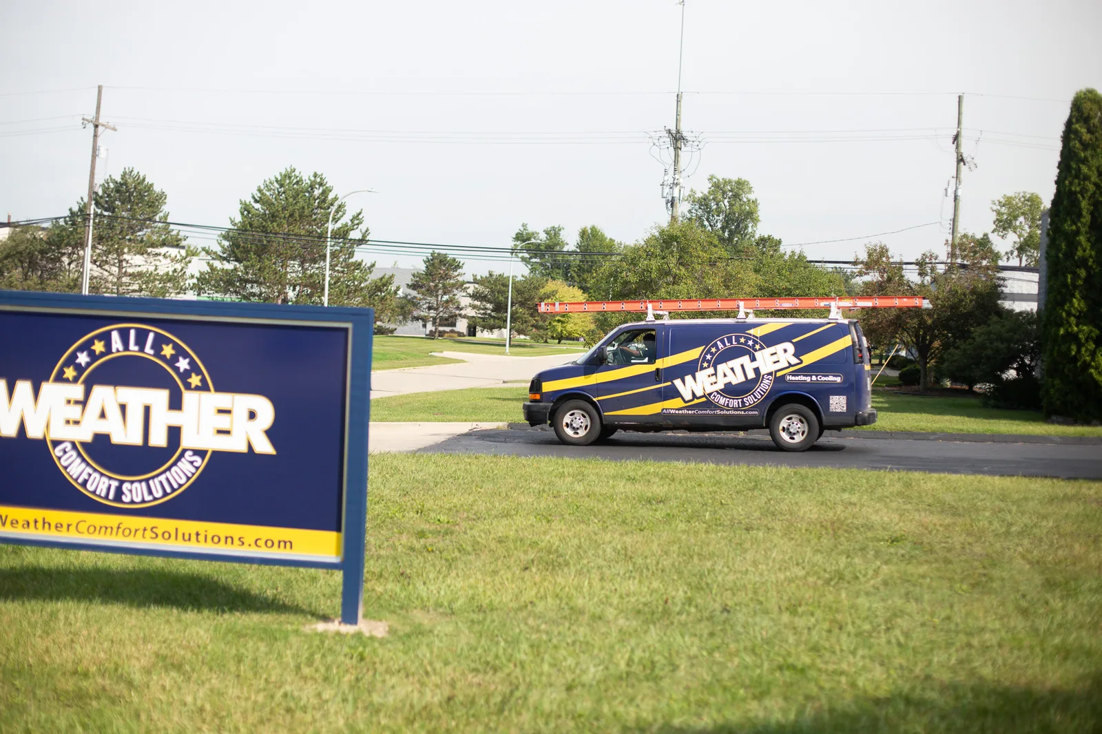 An All Weather van parked on the lawn near the company's roadside sign