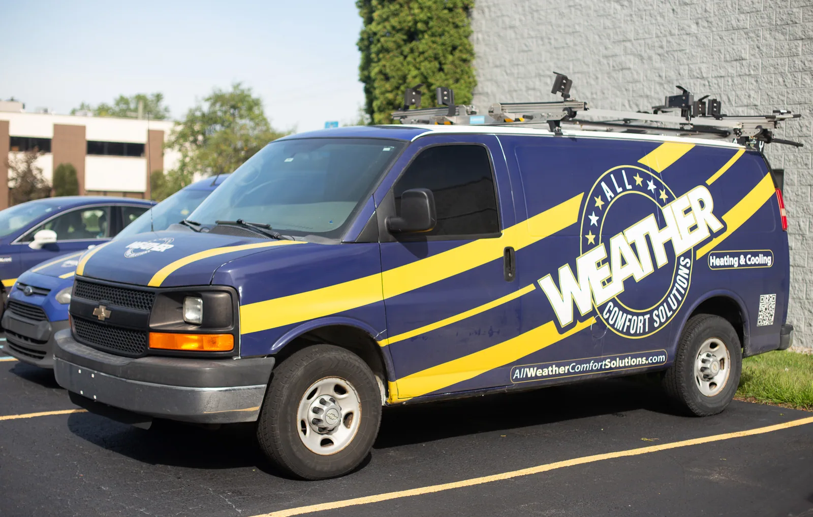 An All Weather Comfort Solutions service van with navy and gold branding outside the shop